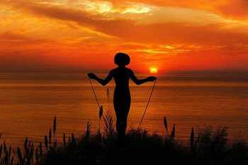 Frau mit Springseil im Sonnenuntergang vor dem Meer