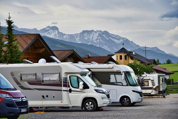 Mehrere Wohnmobile auf einem Parkplatz vor den österreichischen Alpen