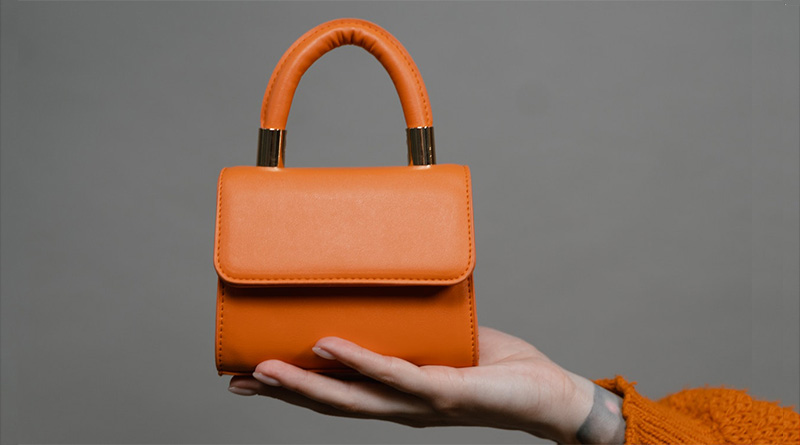 Frauenhand, die eine orange hochhältHandtasche