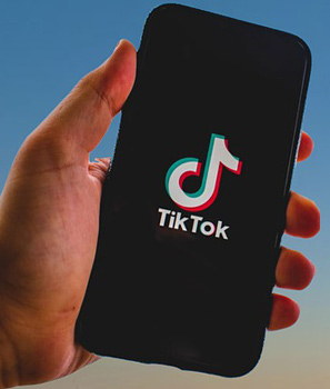 Hand hält ein Smartphone auf dem die TikTok-App zu sehen ist.