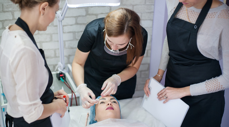 Permanent Makeup Trainerin zeigt 2 Schülerinnen, wie Augenbrauen tätowiert werden