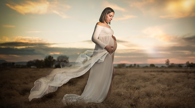 Schwangere Frau im weißen Kleid im Sonnenuntergang