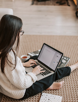 Junge Frau sitzt auf dem Boden und arbeitet am Computer