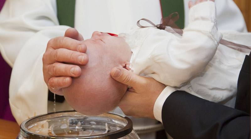 Baby, das von einem Pfarrer über dem Taufbecken getauft wird