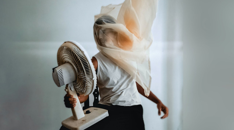 Person mit wehendem Tuch über dem Kopf hält sich einen Ventilator vor den Körper