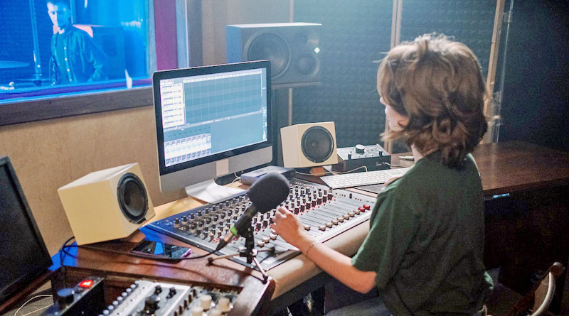 Studentin am Mischpult in einem Tonstudio, Sänger im Hintergrund