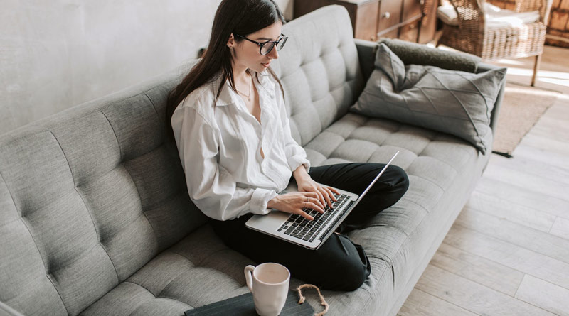 Junge Frau sitzt auf dem Sofa und bewirbet sich über ein Job-Portal online