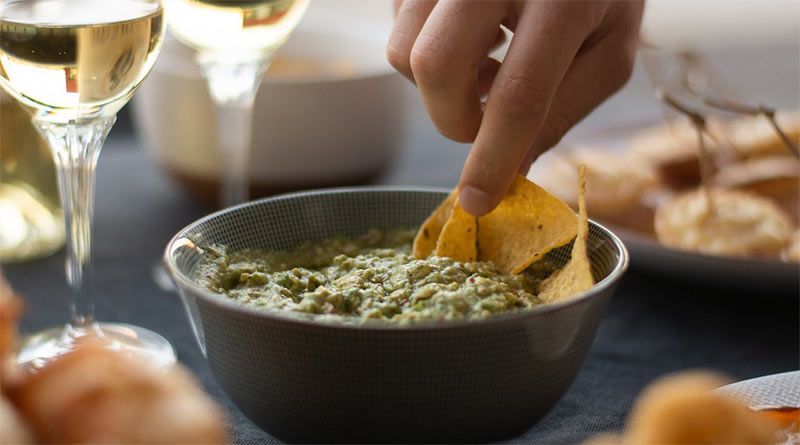 Frau dippt Tortilla-Chip in eine Guacamole