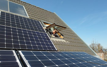 Junge schaut aus einem Dachfenster auf die Solarmodule auf dem Dach