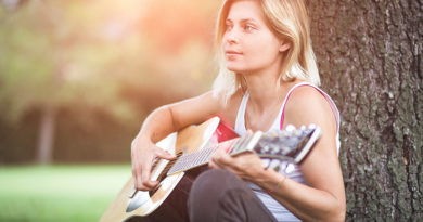 Junge Frau, die im Grünen an einen Baum gelehnt, Gitarre spielt.