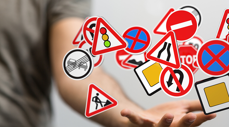 Eine Hand, die viele verschiedene Verkehrsschilder scheinbar jongliert.