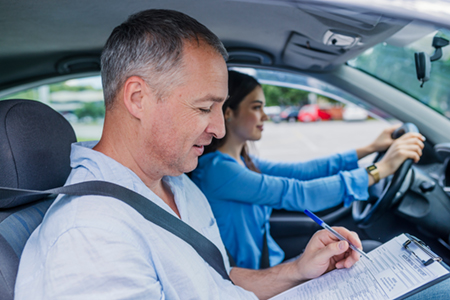 Ein Fahrlehrer mit seiner Fahrschülerin in einem Auto, der praktische Tipps gegen Prüfungsangst gibt.