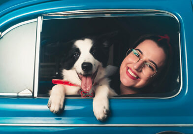 Auto mit geöffnetem Fenster, aus dem ein Hund und eine junge Frau hinausschauen