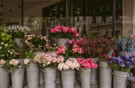 Blumensträuße in Metallgefäßen vor einem Blumenladen.