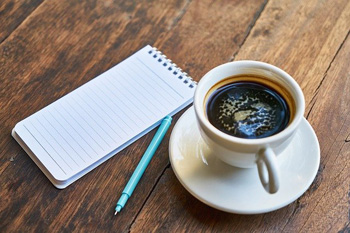 Tisch, auf dem ein Notizblock und eine Tasse Espresso stehen