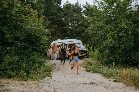 Mehrere junge Menschen, die mit einem Wohnmobil Urlaub machen und nun auf dem Weg zu einem Strand oder Seeufer sind