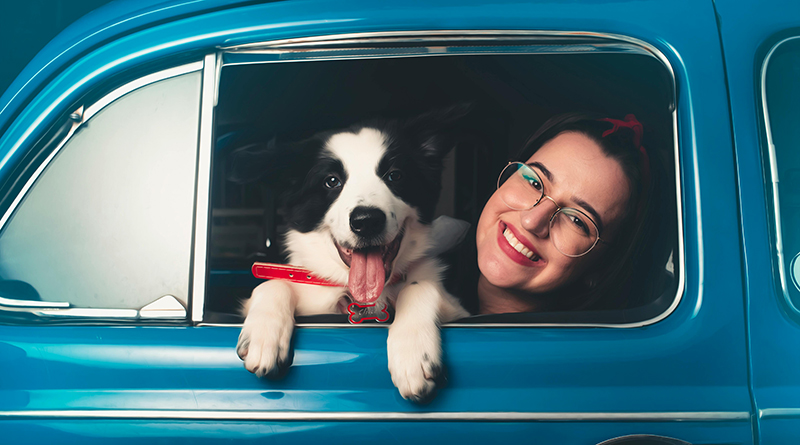 Auto mit geöffnetem Fenster, aus dem ein Hund und eine junge Frau hinausschauen