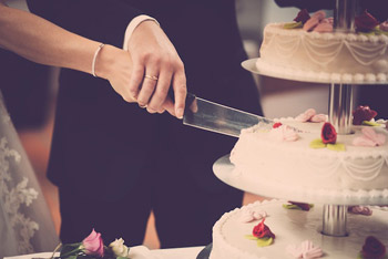 Nahaufnahme von Händen eines Brautpaares, das Hochzeitstorte anschneidet